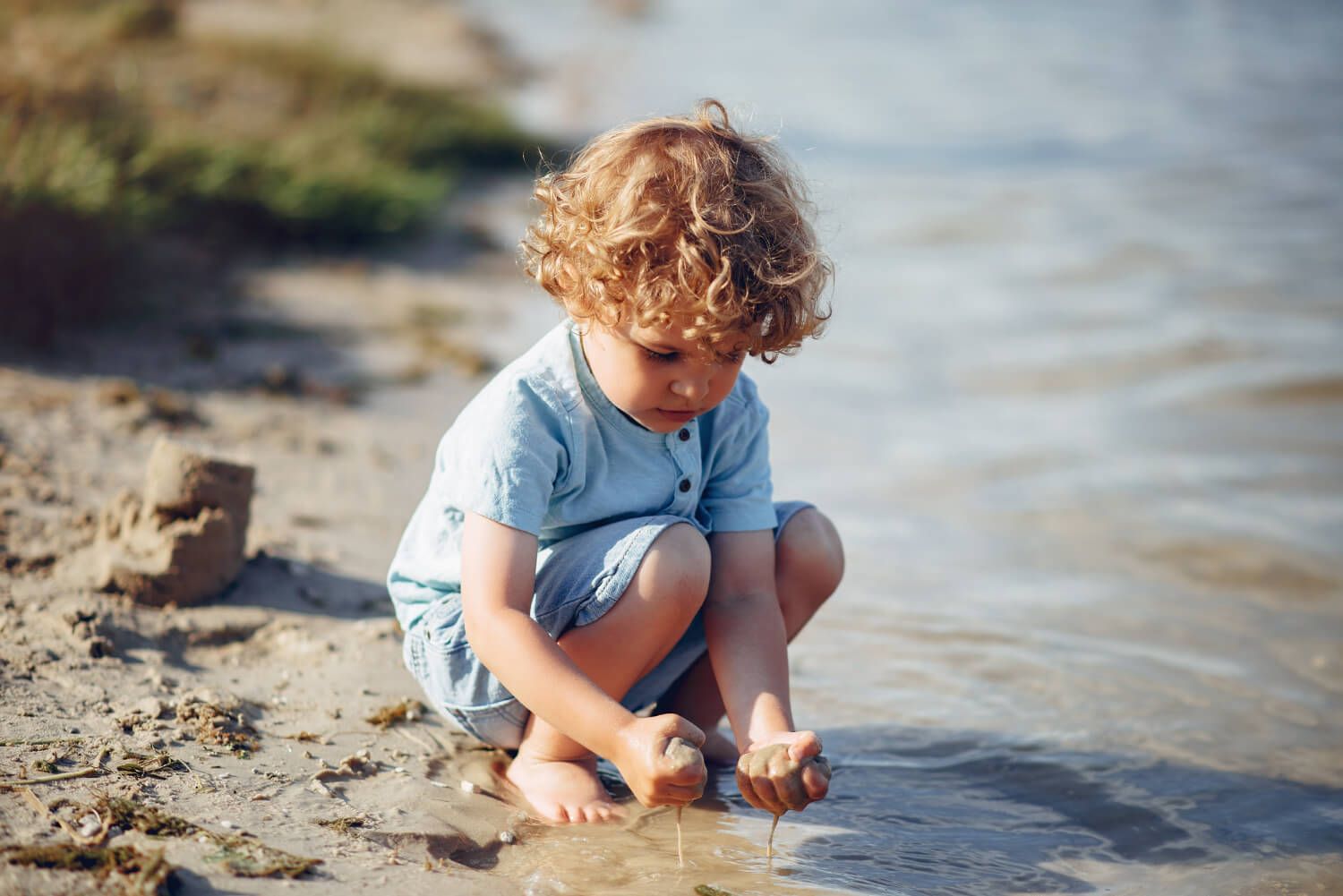chłopiec na plaży, budujący zamek z piasku