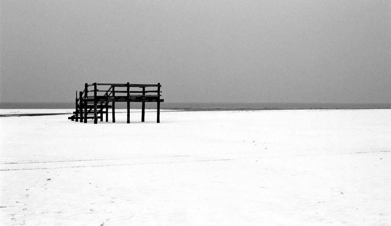 Czarno-biała fotografia drewnianych schodów na pokrytej śniegiem plaży zimą na Półwyspie Helskim